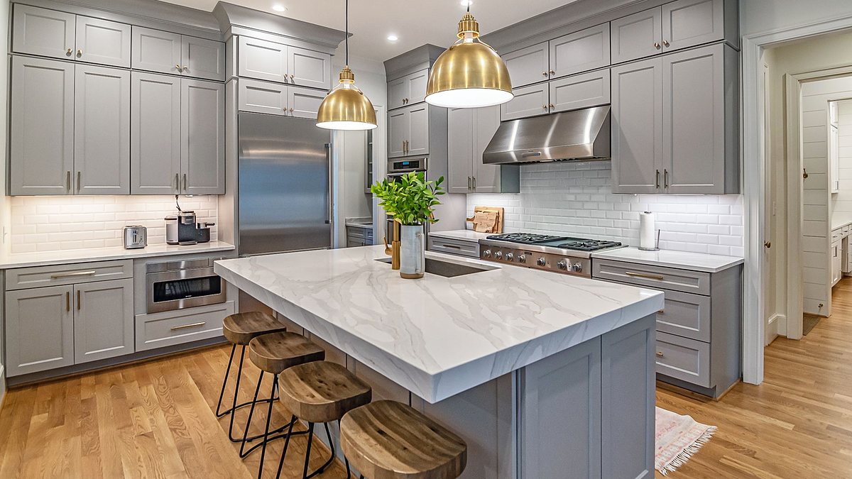 Stylish modern kitchen with a large marble island, gold pendant lights and gray cabinetry