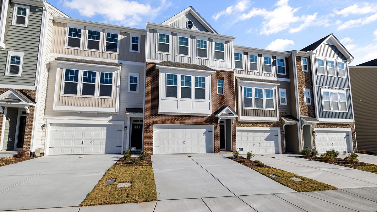 Row of modern suburban townhouses with clean driveways under a blue sky