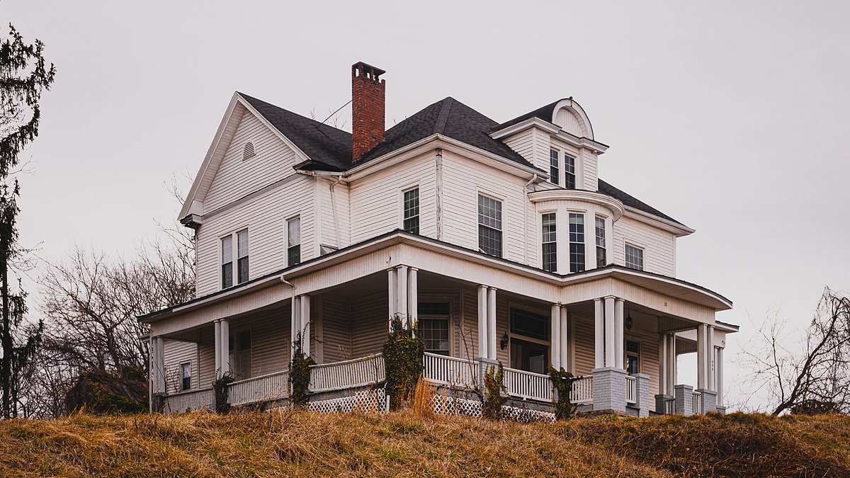 Historic white house with a wraparound porch set against autumn surroundings