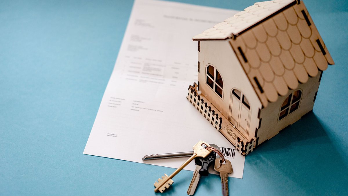 Miniature wooden house with keys and a contract on a table