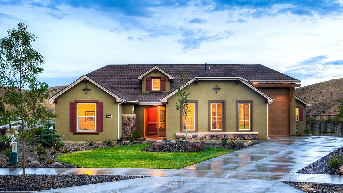 Beautifully illuminated modern beige home with a lush lawn and wet driveway