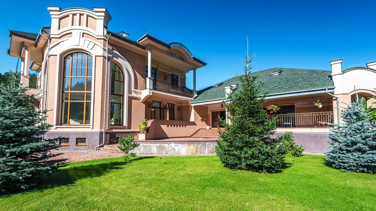 Modern luxury villa with large windows surrounded by a lush green lawn and trees