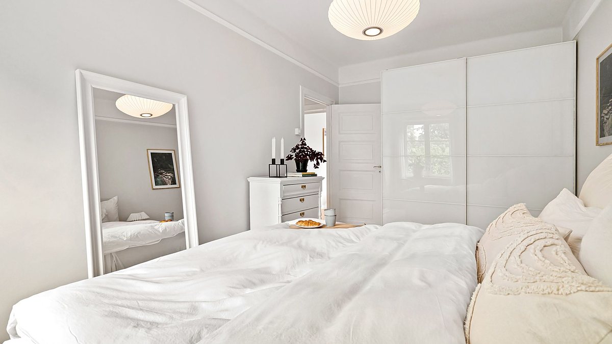Minimalist white bedroom with a bed, dresser and mirror under soft lighting