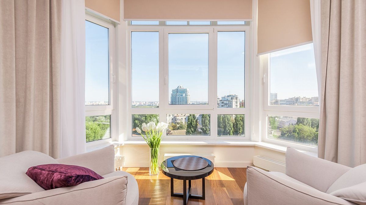 Modern penthouse living room with white armchairs and a round side table beside windows overlooking the city