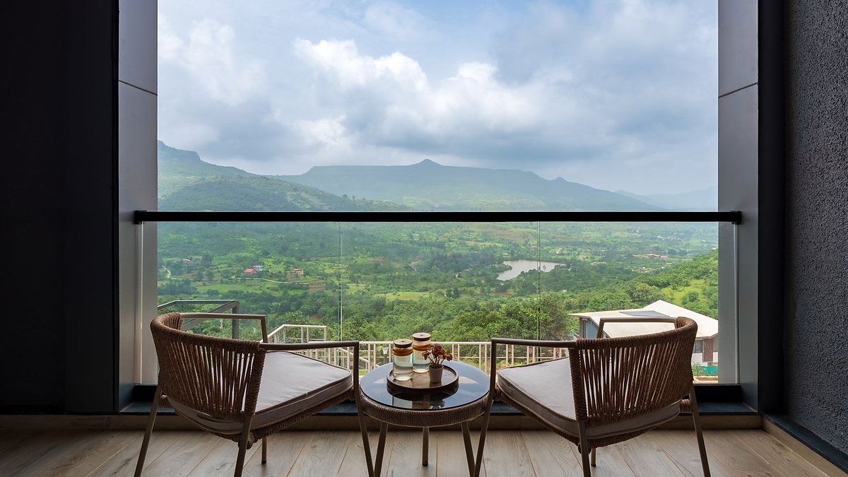 Balcony with two chairs and a table overlooking lush mountains under a cloudy sky