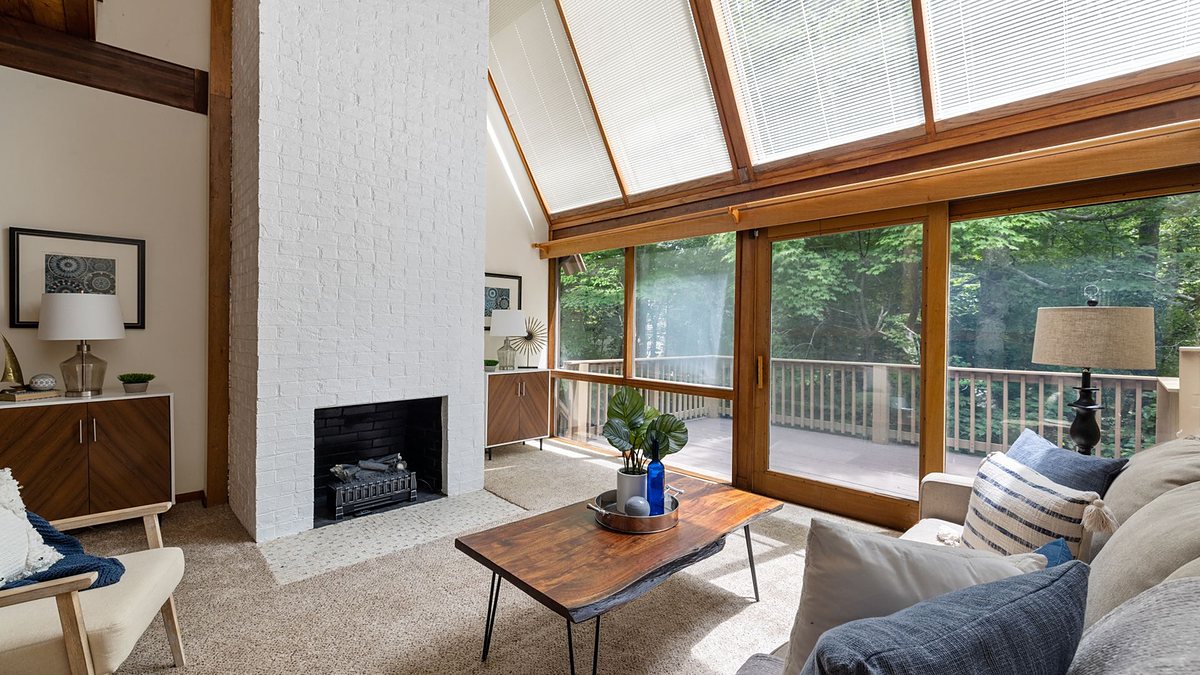 Spacious living room with a white brick fireplace and floor-to-ceiling windows overlooking greenery