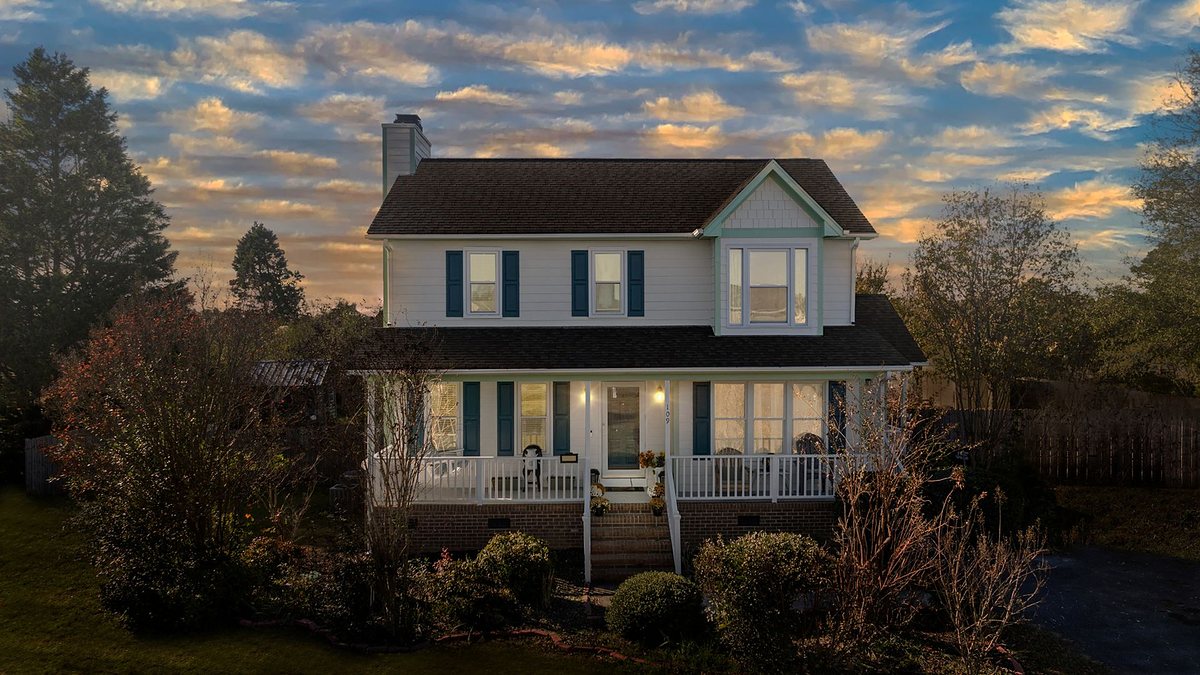 Two-story suburban house with a cozy front porch under a sunset sky